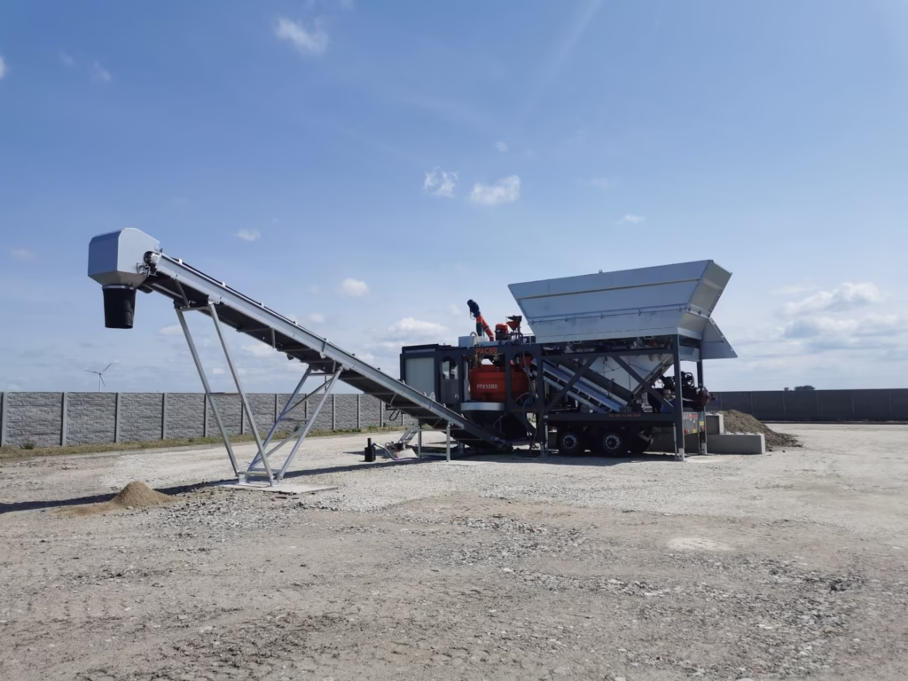Mobile concrete batching plant with twin aggregate hoppers and a long inclined conveyor belt for on-site material transfer.