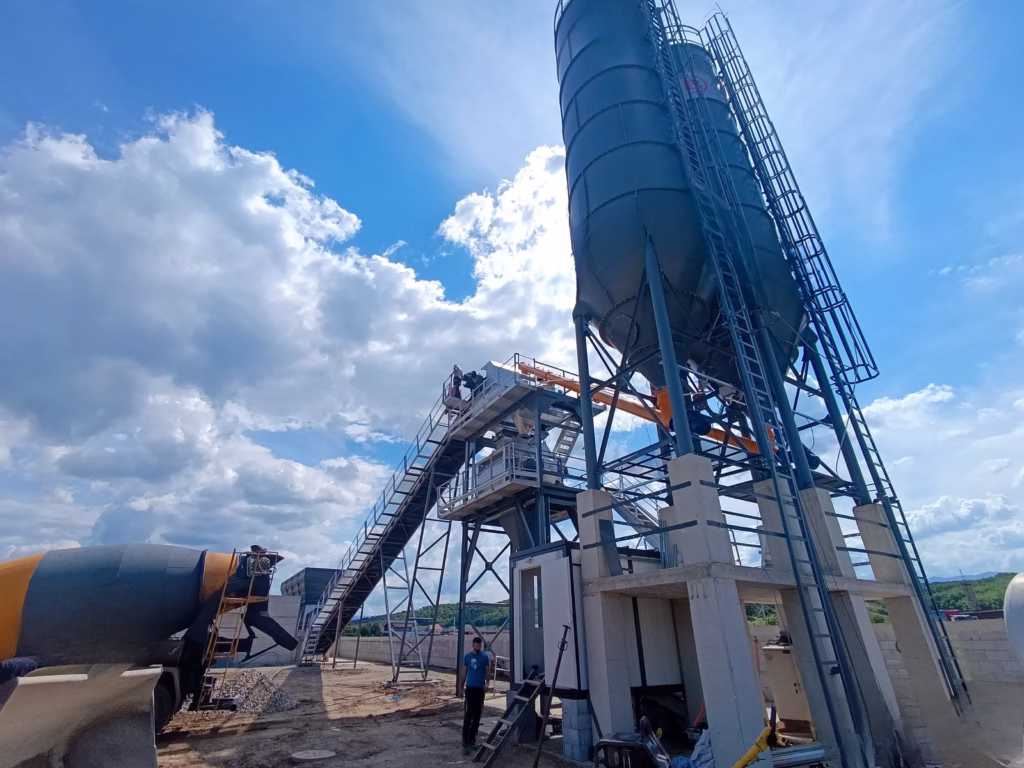 Large blue cement silo with workers on an elevated platform at a concrete batching plant under a blue sky